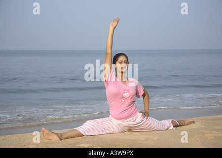 Woman doing sitting yogic stretching exercises on beach enjoying sun sand sea Stock Photo