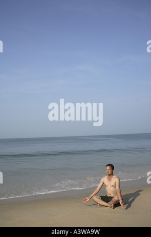 Bachelor on holiday exercising doing sitting  yogic asanas on the beach enjoying sun sand sea Stock Photo