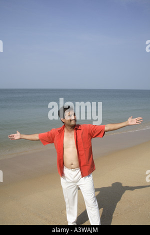 Man standing confidently with hands in the air showing freedom on the clean sand sea beach Stock Photo