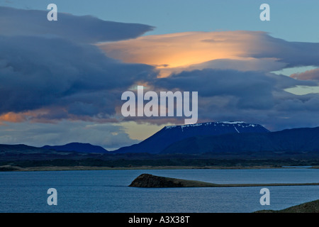 View across Myvatn at dusk towards snow topped volcanic mountain Clouds backlit by setting sun Iceland Stock Photo