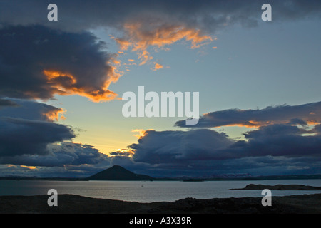 View across Myvatn at dusk towards a rootless cone hill Clouds rim lit by setting sun Iceland Stock Photo