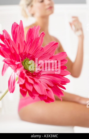 Close up of a flower with a young woman spraying perfume in the background Stock Photo