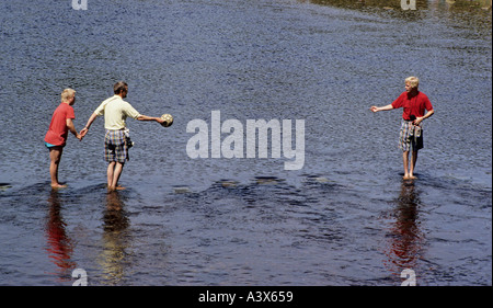 three people crossing a river via stepping stones one person is gesturing to another for help Bolton Abbey in Yorkshire across the River Wharfe Stock Photo