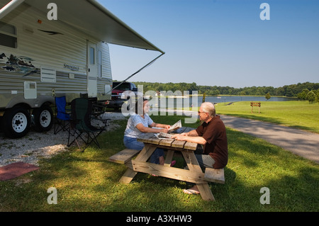 Senior Couple Enjoying the Newspaper While Sitting at Picnic Table In Front of Their Camper Overlooking a Lake Buffalo Trace Par Stock Photo