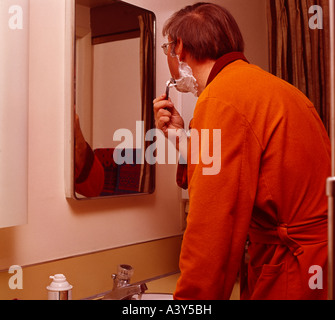 Young man shaving in his bathroom before the mirror Stock Photo