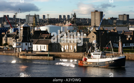 A fishing boat leaving Aberdeen Harbour with Fittie and Aberdeen skyline in background Stock Photo