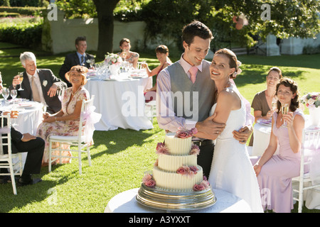 Mid adult bride and groom in garden among wedding guests, holding wineglasses, embracing Stock Photo