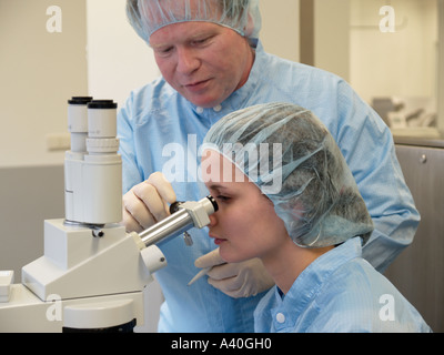 Experienced male industry worker helping teaching female novice coworker with inspecting product sample using a microscope Stock Photo