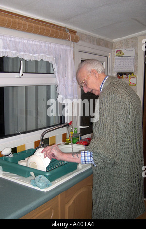Senior male doing domestic chores in the kitchen washing up dirty crockery Stock Photo