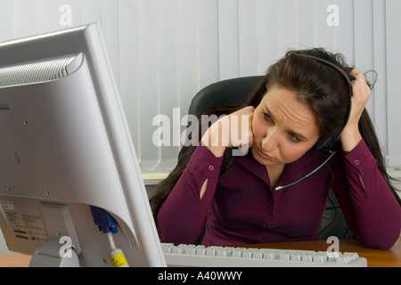 confused young female secretary or office worker using computer with headphones Stock Photo