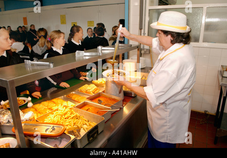 School pupils queue at hot counter waiting to be served by kitchen staff in school refectory UK