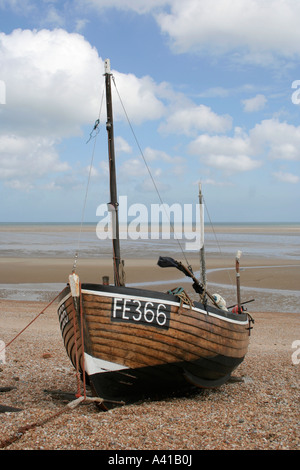 Old wooden UK fishing pulled onto the beach at Greastone-on-Sea in Kent with fluffy clouds behind Stock Photo