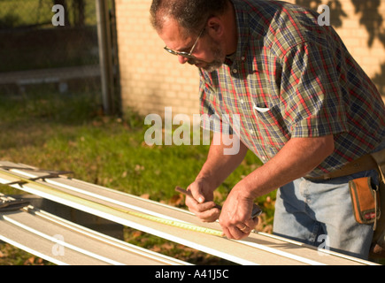 Installer measures and marks vinyl siding for cutting during residential exterior renovation project in the USA. Stock Photo