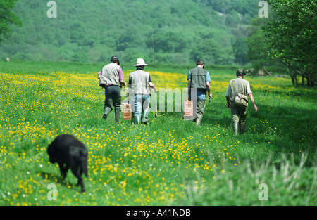 England Devon Fly fishermen carry their rods through the geen fields of the village of Lifton Stock Photo