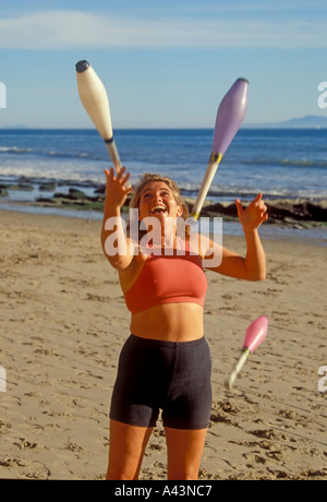 A deft young lady juggles with Indian clubs in afternoon sun on the beach at Santa Barbara California USA Stock Photo