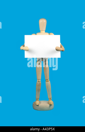 Wooden mannequin holding a blank white piece of card against a sky blue background space on the card for text Stock Photo