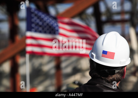 Construction Foreman Wearing Hard hard hat with American Flag Looking Over Job Site With Flag in Distance Stock Photo