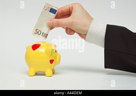 Businesswoman holding fifty euro banknote over piggy bank Stock Photo