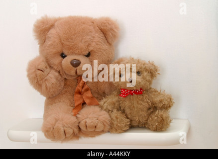 Big teddy bear and little scruffy teddy bear sitting side by side on nursery shelf Stock Photo