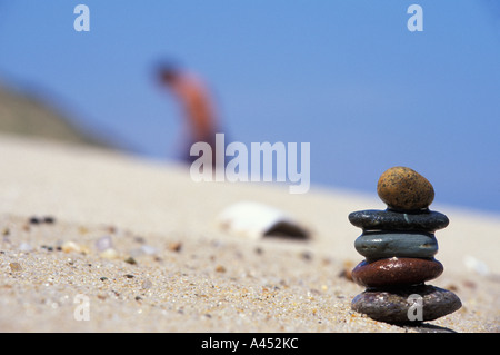 Miniature cairn piled on Cape Cod Beach, with beach goer in the background, MA Stock Photo