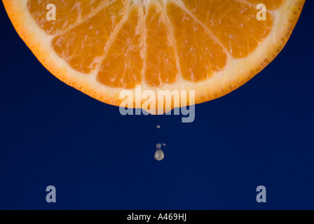 Drops of juice falling from freshly cut orange isolated on a blue background Series Stock Photo