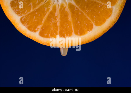 Drops of juice falling from freshly cut orange isolated on a blue background Series Stock Photo