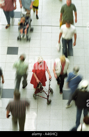 Old woman with a walker standing between hurrying people Stock Photo