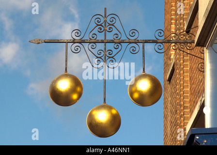 Pawn shop business close up of traditional sign of three gold balls above Pawnbroker shop premises supported on ornamental iron bracket England UK Stock Photo