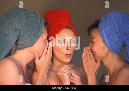 Three women of ethnic mix with colorful bath towels sharing gossip Stock Photo