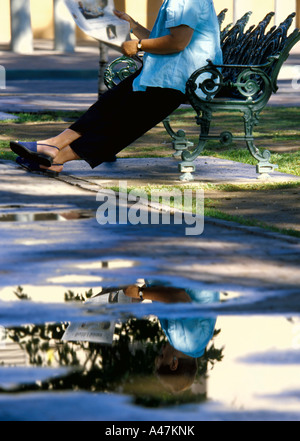 Woman reading on park bench with puddles Stock Photo