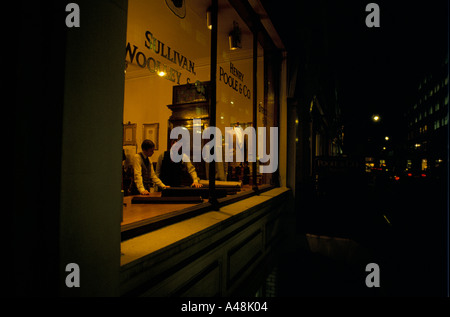tailor shop on saville row london shopkeeper customer choosing fabric behind shop window at night Stock Photo