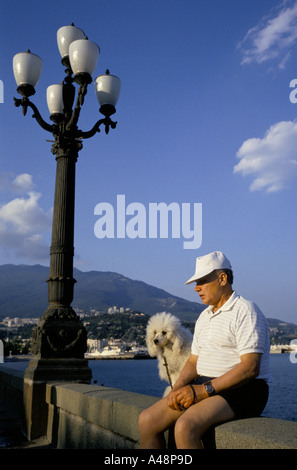 A middle aged man and his dog sitting in the sun on Yalta seafront .crimea .ukraine Stock Photo