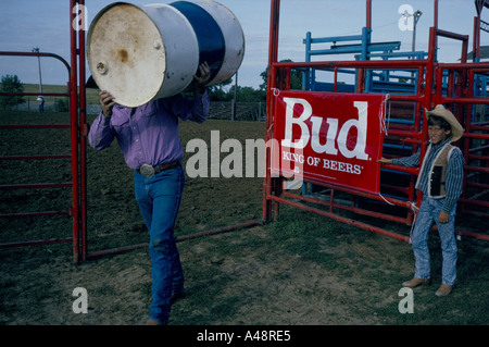 Cowboy carrying an oil drum preparing the ring for a rodeo in iowa usa  watched by a young rodeo fan Stock Photo