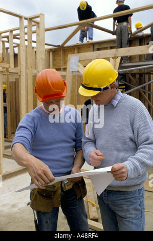 construction workers looking at plans while other builders working on timber structure in background Stock Photo