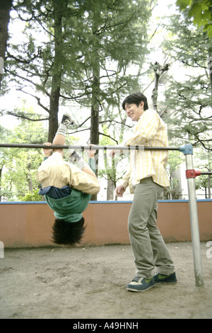 Boy hanging on monkey bars with his father standing beside him Stock Photo