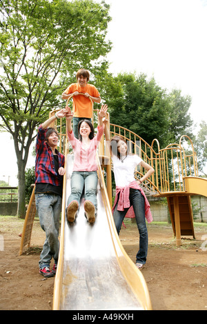 Young woman sliding on a slide with her friends standing beside her Stock Photo
