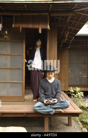 Young man reading a book with a young woman standing at the door Stock Photo