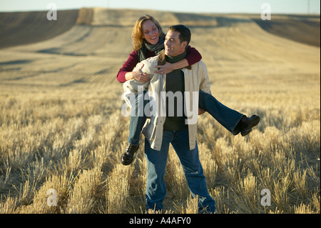 Woman laughing on mans back in cut grass fields in Fall Colorado Stock Photo