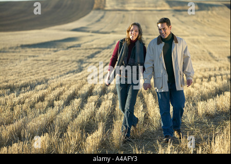 Couple smiling holding hands walking through fields of cut golden grass in Fall Colorado early morning Stock Photo