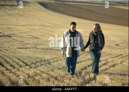 Couple smiling holding hands walking through fields of cut golden grass in Fall Colorado early morning Stock Photo