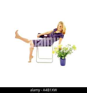 young woman siting playfully on chair with flowers on the floor in white studio Stock Photo