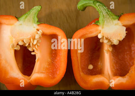 Two red pepper halves showing the inside with seeds placed on a wooden cutting board Stock Photo