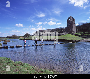 Group of girls crossing stepping stones over the river Ewenny to Ogmore Castle in the Vale of Glamorgan, Wales set against a blue sky with wispy cloud Stock Photo