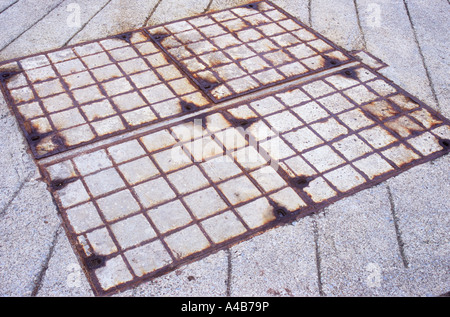 Close up of a grid of four large square iron and cement manhole covers set in a large expanse of concrete
