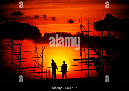 Two workmen silhouetted against setting sun working at height on a building construction site Cardiff Wales UK Stock Photo