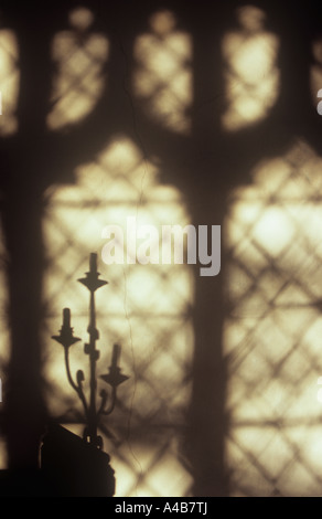 Projection in warm light onto wall of three-headed candlestick and 15th century Gothic Perpendicular window with plain glass Stock Photo