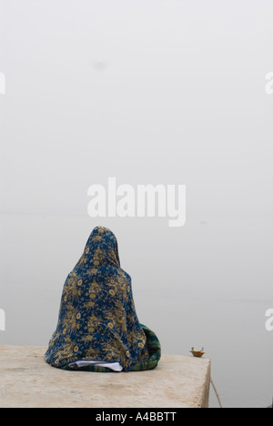 Indian woman wrapped in her sari with her head covered contemplating or meditating on the banks of the Ganges at Varanasi Stock Photo