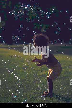 A 24 month old girl plays with bubbles in a grassy field Stock Photo