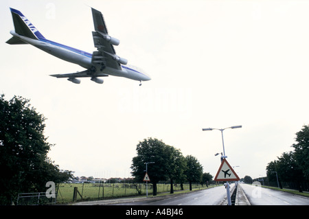 Aircraft coming in to land at London Heathrow airport flies over A4 past a sign warning of low flying aircraft near Hatton Cross Stock Photo