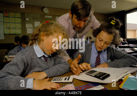 A teacher helps two girls during a maths class at a state seconday school Stock Photo